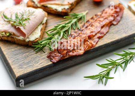 Frische, leckere Sandwiches mit Schinken, Butter, Avocado und Sesam auf einem Holzbrett. Leckere gesunde Lebensmittel Stockfoto