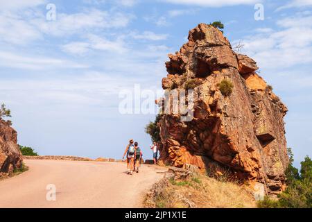 Korsika, Frankreich - 23. August 2018: Touristen wandern in Calanques de Piana in der Nähe von massivem rotem Stein, der an einer Straße steht Stockfoto