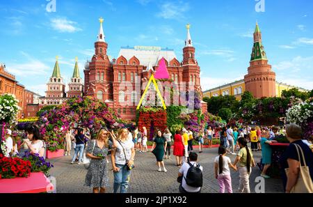 Moskau - 2. Aug 2022: Blumenfest auf dem Manezhnaya-Platz, Moskau, Russland. Historisches Museum und Kreml in der Ferne. Die Leute laufen an schönen Blumen vorbei Stockfoto