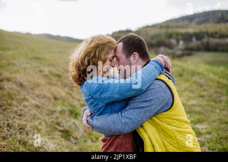 Outdoor-Porträt der Mutter umarmt ihren erwachsenen Sohn mit Down-Syndrom, Mutterschaft Konzept. Stockfoto