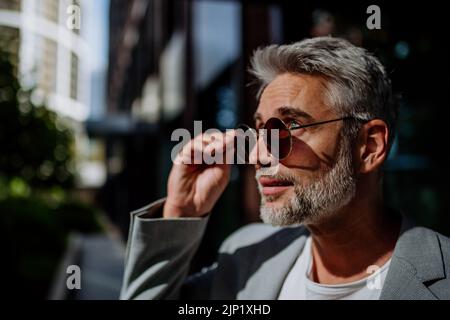 Porträt, Seitenansicht eines reifen Geschäftsmanns in Sonnenbrillen, der auf der Straße steht. Stockfoto