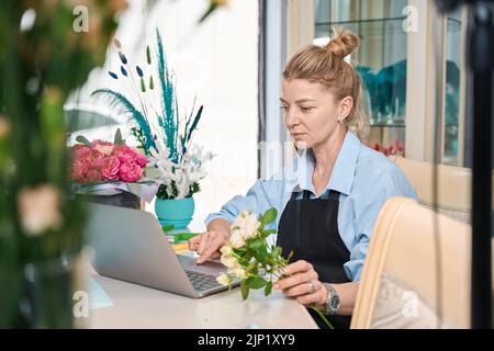 Der Florist sitzt während eines Online-Workshops vor einem offenen Laptop Stockfoto