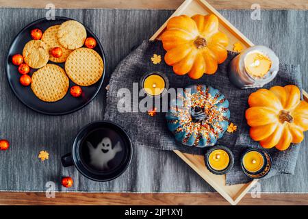 Draufsicht Herbstkomposition für Halloween. Orangefarbene und graue Kürbisse, brennende Kerzen auf dem Tablett und Teller mit halloween-Süßigkeiten und heißem Tee mit Geist Stockfoto