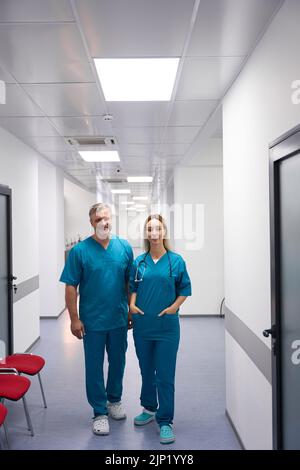 Zwei Ärzte stehen im Flur und schauen lächelnd auf die Kamera Stockfoto
