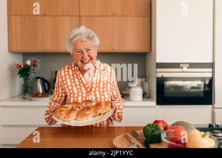 Glückliche ältere Frau mit hausgemachtem süßen geflochtenen Brot mit Rosinen. Stockfoto