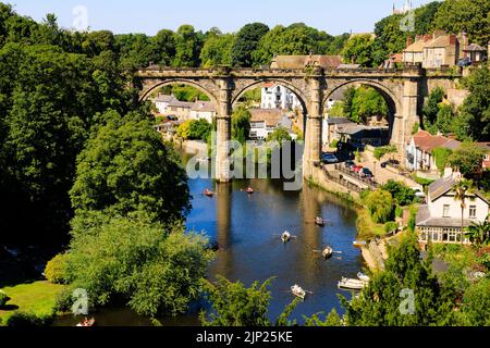 Der Eisenbahnviadukt über den Fluss Nidd, Knaresborough, North Yorkshire, England. Heißer Sommertag mit Menschen auf Booten im Fluss. Stockfoto