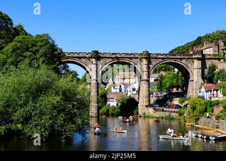 Der Eisenbahnviadukt über den Fluss Nidd, Knaresborough, North Yorkshire, England. Heißer Sommertag mit Menschen auf Booten im Fluss. Stockfoto