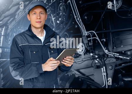 Servicearbeiter mit digitalem Tablet auf dem Hintergrund des Traktors mit offener Motorhaube Stockfoto
