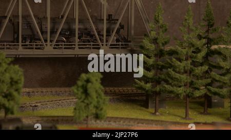 Dampflokomotive Spielzeug über die Brücke. Vintage-Spielzeugzug, der auf einer Eisenbahn durch den Wald in den Bergen fährt. Fun-Spiel für Kinder. Stockfoto