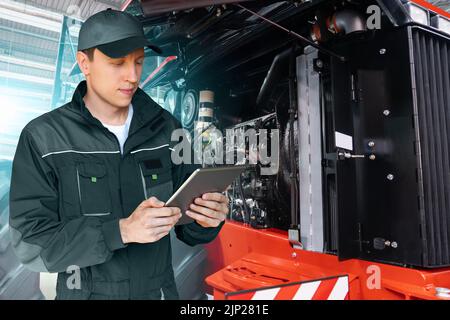 Servicearbeiter mit digitalem Tablet auf dem Hintergrund des Traktors mit offener Motorhaube Stockfoto