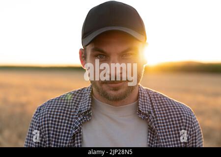 Bärtiger Bauer in einer Mütze und einem karierten Hemd vor dem Hintergrund eines Feldes Stockfoto