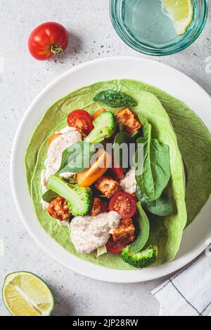 Offener veganer grüner Tortilla-Wrap mit Brokkoli, Tofu und Tomaten, Draufsicht. Vegetarisches Rezept, Comfort Food, pflanzliches Konzept. Stockfoto