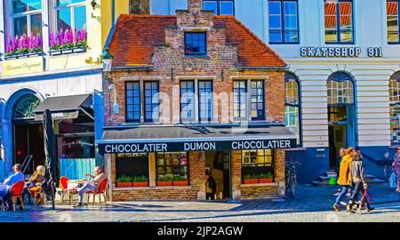 Brügge, Belgien - Oktober 9. 2021: Blick über die Einkaufsstraße auf alte, isolierte, mittelalterliche Backsteinhaus-Chocolatier zwischen modernen Gebäuden Stockfoto