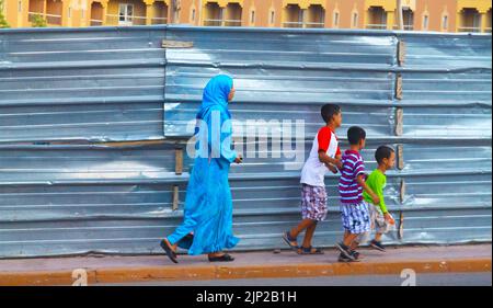 Marrakesch, Marokko - Mai 9. 2015: Alleinerziehende muslimische Mutter mit 3 Kindern, die in einer Reihe am Metallzaun des neuen Wohngrundstücks auf AP vorbeigehen Stockfoto