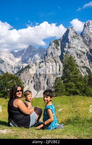 Eine Mutter mit ihren beiden Söhnen sitzt auf grünem Gras in einer bergigen Gegend Stockfoto