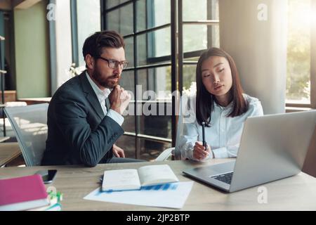 Zwei fokussierte Geschäftsleute, die in einem modernen Büro arbeiten und ein neues Projekt diskutieren Stockfoto