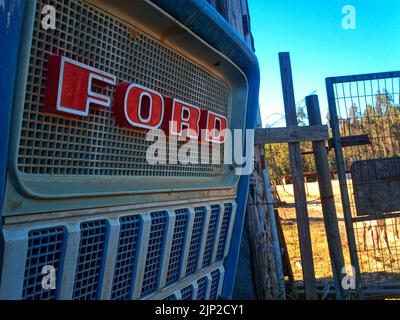 Nahaufnahme eines roten Ford-Logos auf einem alten Feldarbeitsschlepper neben einem Zaun Stockfoto