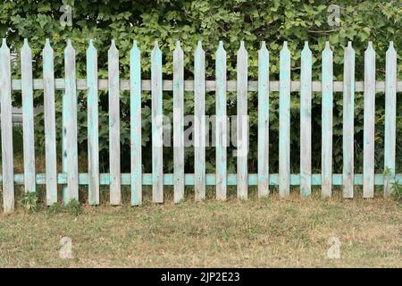 Ein kleiner blauer Holzzaun steht vor dem Hintergrund eines hohen roten Metallzauns Stockfoto