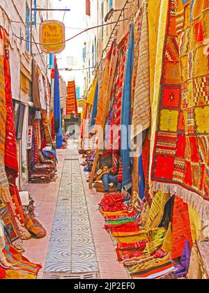 Essaouira, Marokko - Mai 9. 2015: Schmale Medina Gasse mit Geschäften, maroccan bunte Berberteppiche hängen an Hausfassaden zum Verkauf Stockfoto