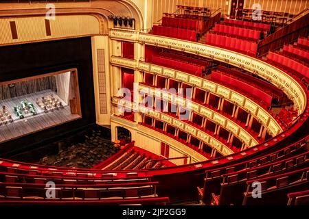 Das Innere der Wiener Staatsoper mit einer hell erleuchteten Bühne und runden Reihen leerer roter Sitze Stockfoto