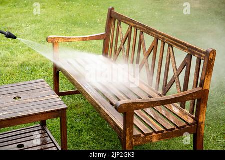 Nahaufnahme der Person arbeiten Reinigung Druck waschen hölzerne Gartenmöbel Bank im Freien im Sommer. Stockfoto