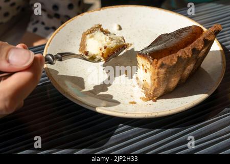 Die Hand der Frau mit einem Löffel nimmt ein Stück Käsekuchen von einem Teller Stockfoto