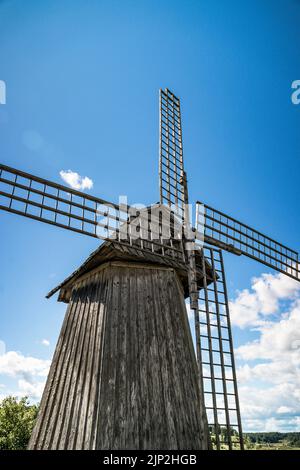 Nahaufnahme der hölzernen Windmühle mit großen Klingen und einem schönen, sonnigen Himmel Stockfoto