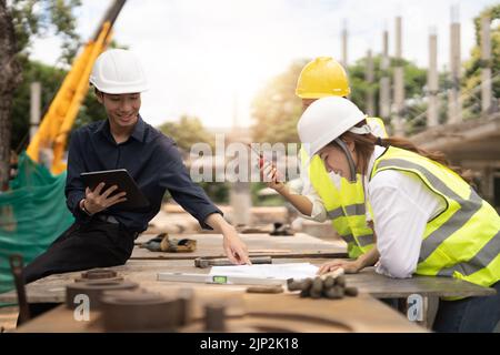 Junge asiatische Architekten und Ingenieure diskutieren auf der Baustelle über Baupläne Stockfoto