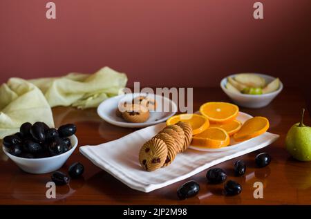Obstteller mit einer Mischung aus frischen, saftigen, süßen Orangen, Birnen, Jamun, auch als Java-Pflaumenbeeren und Haferkekse bezeichnet, die auf einem dunklen Holztisch als B platziert werden Stockfoto