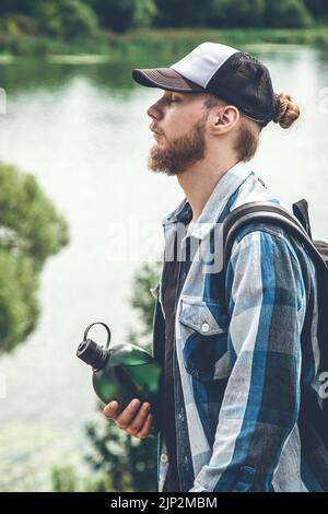Männlicher Reisender mit Rucksack und Karimat in der Natur am See, Tourismuskonzept. Stockfoto