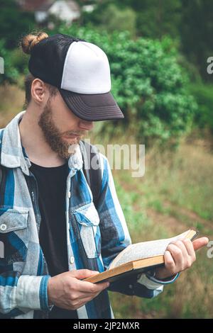 Ein Mann in einem karierten Hemd liest in der Natur ein Buch. Stockfoto