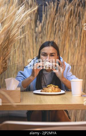 Eine junge Frau isst Croissants mit Kaffee in einem Café. Stockfoto