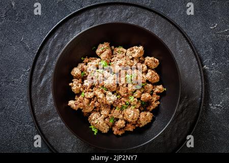 Nahaufnahme von gebratener italienischer Wurst aus frisch gemahlenem Schweinefleisch und Gewürzen in schwarzer Schüssel auf Betontisch, flach liegend Stockfoto