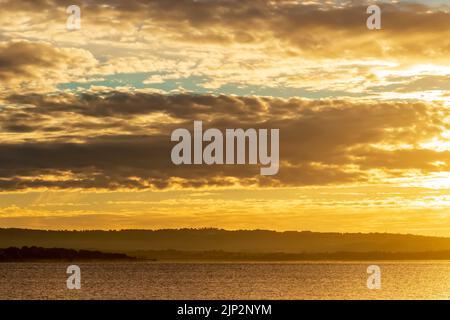 Sonnenuntergang über dem See, Spiegelung der Sonne mit Wolken, dramatischer Himmel und goldenen Farben. Manzanares Madrid. Stockfoto