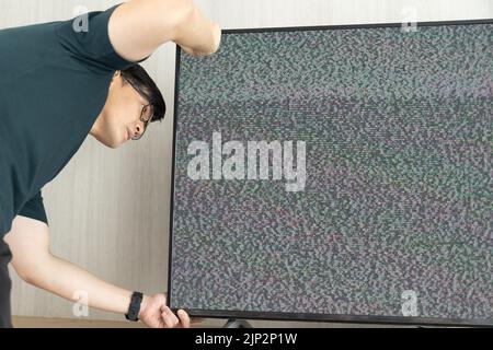 Ein Mann repariert Fernsehen verloren Signalrauschen auf dem Bildschirm suchen Kabel verstecken Stockfoto