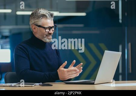 Ältere ältere ältere grauhaarige Mann mit Laptop Remote-Kommunikation Geschäftstreffen erfahrene Geschäftsmann in Brille arbeiten modernen Büroinvestor lächelnd sprechende Kollegen. Stockfoto