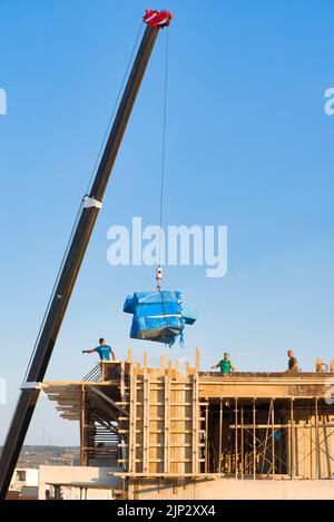 Bauarbeiter entladen Baumaterialien von einem Kran Stockfoto