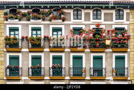 Fassade eines Hauses mit Balkonen voller Blumen in der Stadt Hondarribia im Baskenland. Spanien. Stockfoto