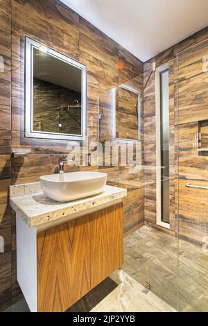 Badezimmer mit luxuriösen Oberflächen, Hauptspiegel mit LED-Licht von hinten, weißes Keramikwaschbecken Stockfoto