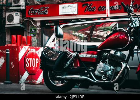 Eine schöne Aufnahme eines roten Motorrads auf dem Hintergrund eines Coca Cola-Werbespots und eines Stoppschildes Stockfoto