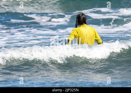 Junge Frau, die auf einem Surfbrett mitten im Meer sitzt Stockfoto