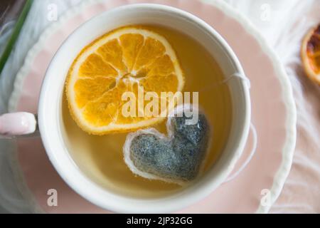 Ein Blick von oben auf einen Tee mit einem herzförmigen Teebeutel und einer Scheibe Orange in einer rosa Tasse Stockfoto