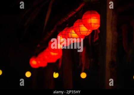 Eine selektive Fokusaufnahme von roten chinesischen Laternen, die auf einem Holzpfahl mit unscharfem Hintergrund hängen Stockfoto