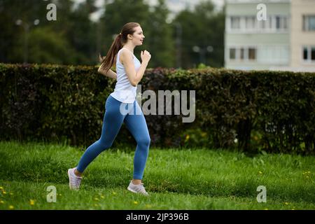 Frau in ihren 30s jogs im Stadtpark am Sommertag. Stockfoto