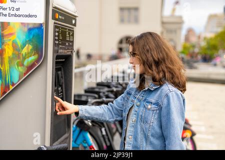 Junge Frau, die ein E-Bike mietet | Fahrradverleih | Transport | Fahrradverleih | ungestellte Porträts Stockfoto