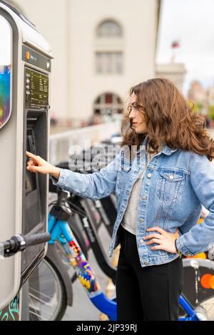 Junge Frau, die ein E-Bike mietet | Fahrradverleih | Transport | Fahrradverleih | ungestellte Porträts Stockfoto