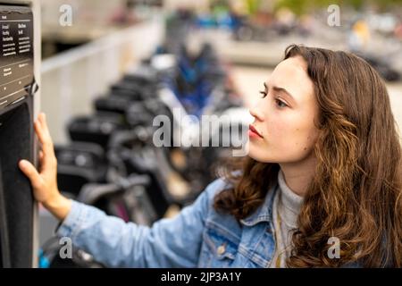 Junge Frau, die ein E-Bike mietet | Fahrradverleih | Transport | Fahrradverleih | ungestellte Porträts Stockfoto