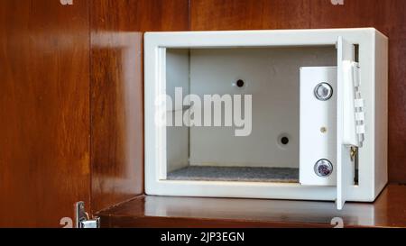 Sicherheit offener Metalltresor mit leerem Platz in einem Holzregal. Weiße Safebox, offene Tür. Safe mit elektronischem Schloss im Hotel oder zu Hause. Sele Stockfoto