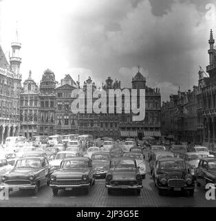 1960s, historische, Autos der Zeit geparkt am Grand-Place, dem historischen zentralen Platz von Brüssel, Belgien. In dieser Zeit konnte man vor den Gebäuden aus dem 17.. Jahrhundert ein Auto parken und so wurde der Stadtplatz zu einem großen Parkplatz. Das Auto war modern, das Auto war König. Anfang 1970s begann ein Artikel des britischen Journalisten John Lambert eine Bewegung, um dies zu ändern, und so wurde im März 1972 von März bis September das Parken von Privatparkplätzen verboten, obwohl Autos noch durch den Platz fahren konnten. Erst 1990 wurde der Platz zur Fußgängerzone, und der Verkehr wurde verboten. Stockfoto