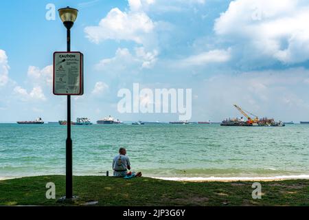 Ein Mann sitzt am Strand und genießt den tropischen Blick auf den East Coast Park, Singapur. Speicherplatz Kopieren. Stockfoto